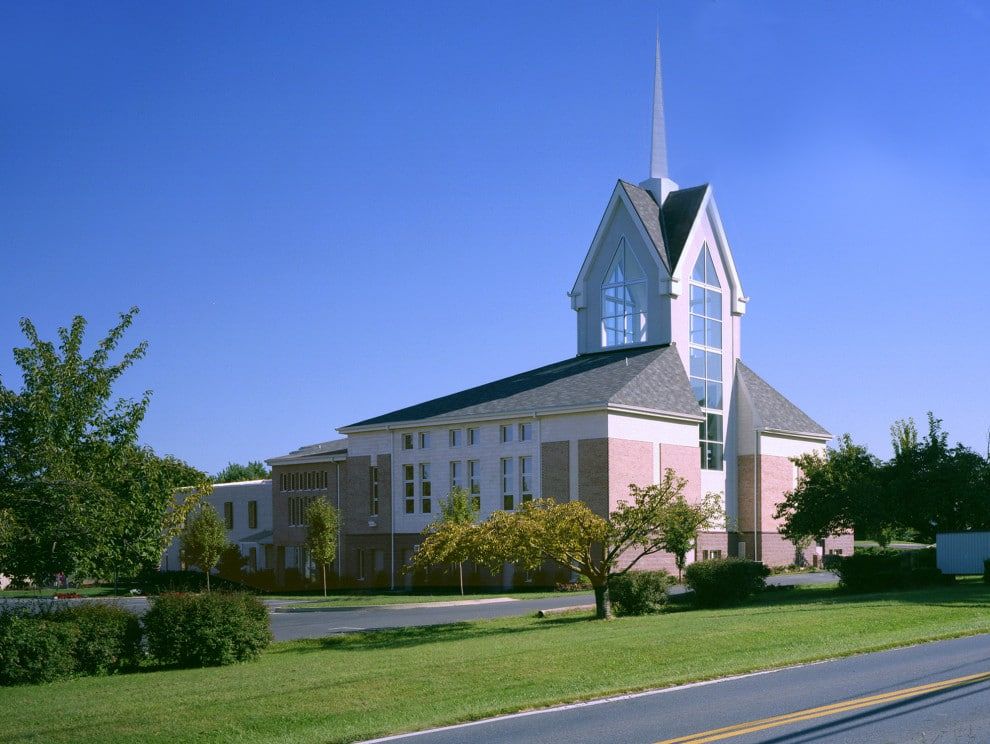 Modern church with white and pink facade and tall steeple beside a road under a blue sky