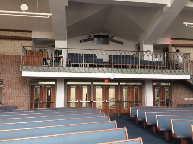 Empty church auditorium with blue pews, balcony seating, and a stage with a lectern.