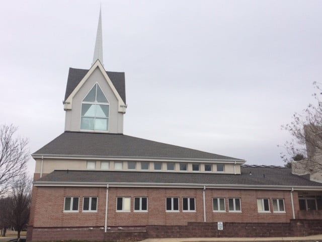 Brick church with a tall white steeple and dark roof under an overcast sky