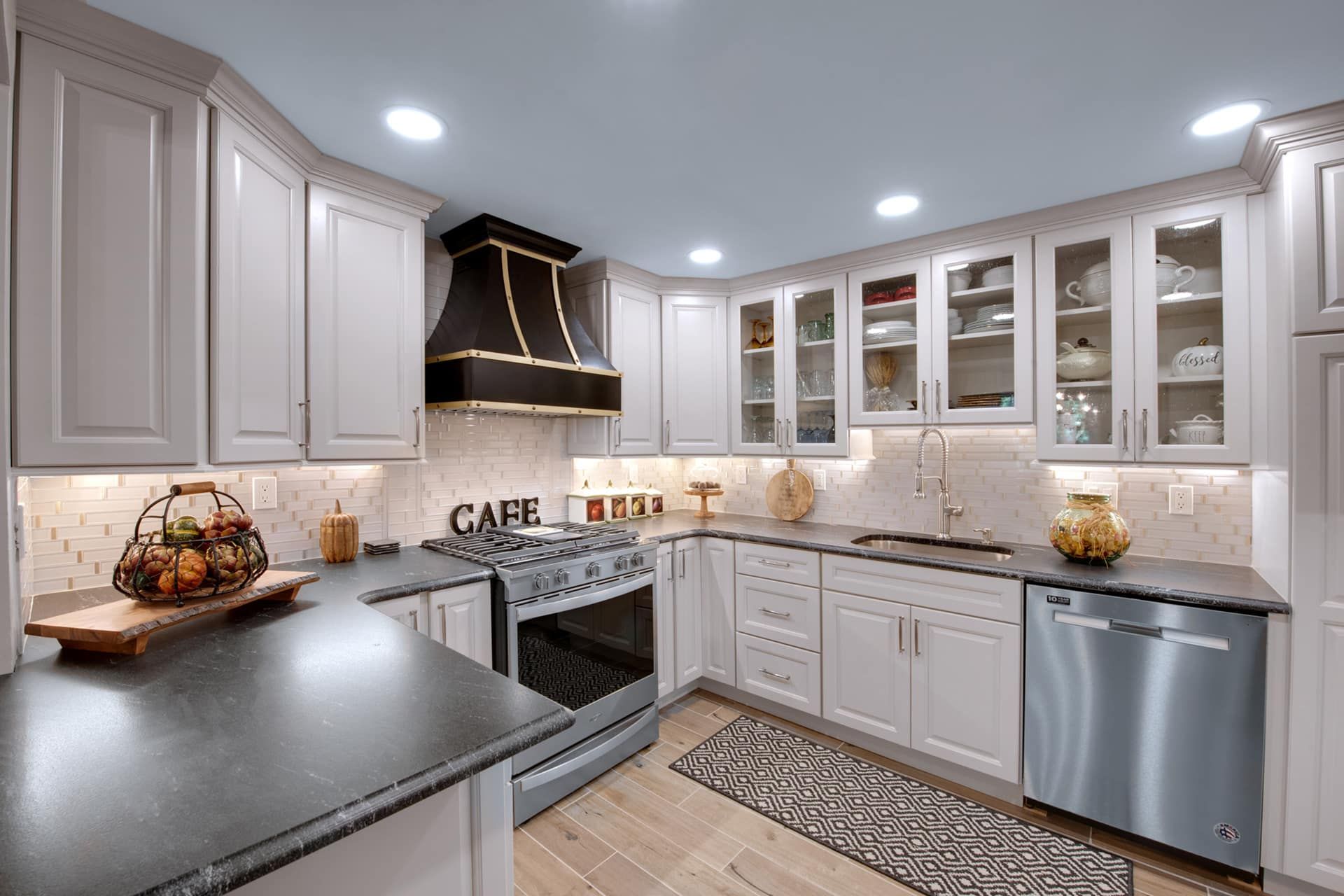 Modern white kitchen with gray countertops, stainless appliances, and black range hood