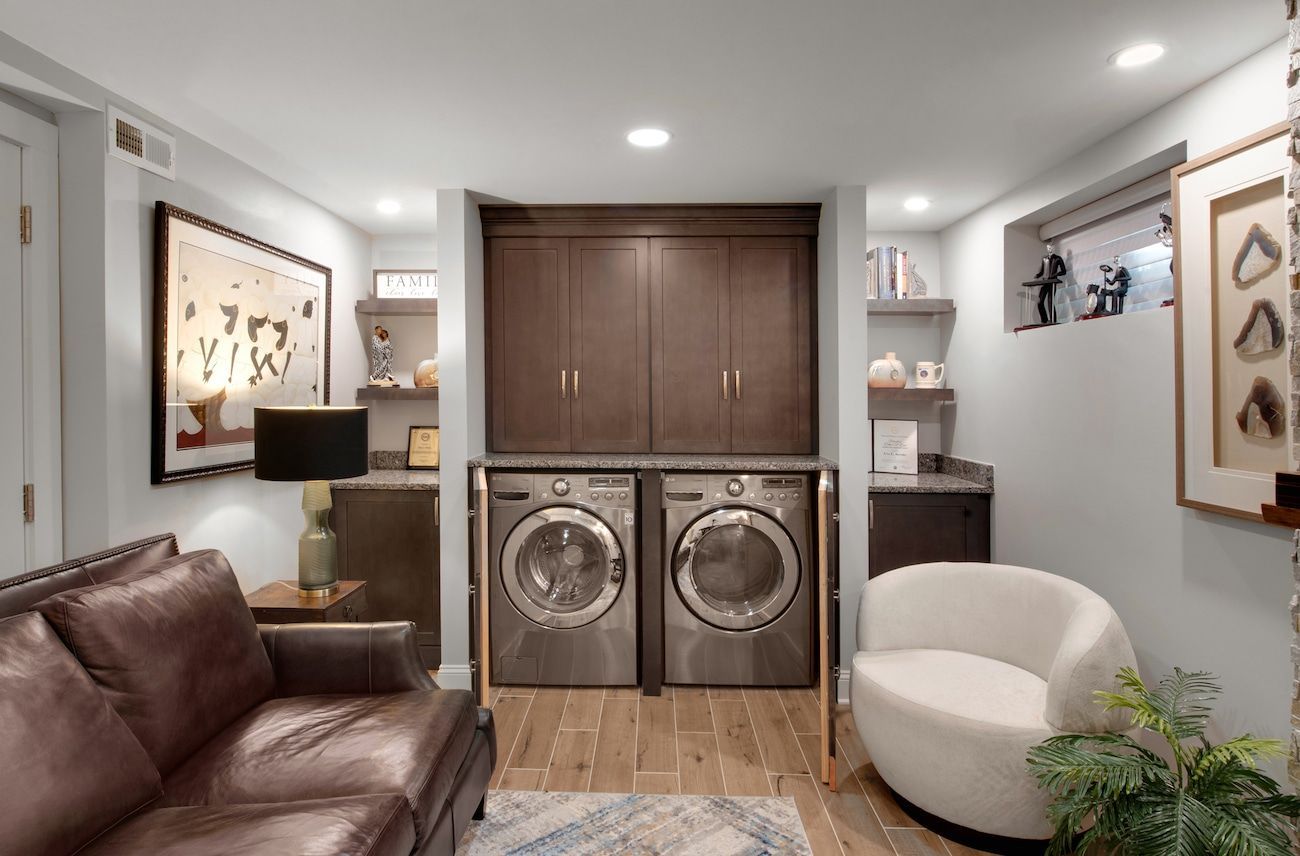 Modern laundry room with stacked washer-dryer in a built-in cabinet, framed by a leather sofa and white chair