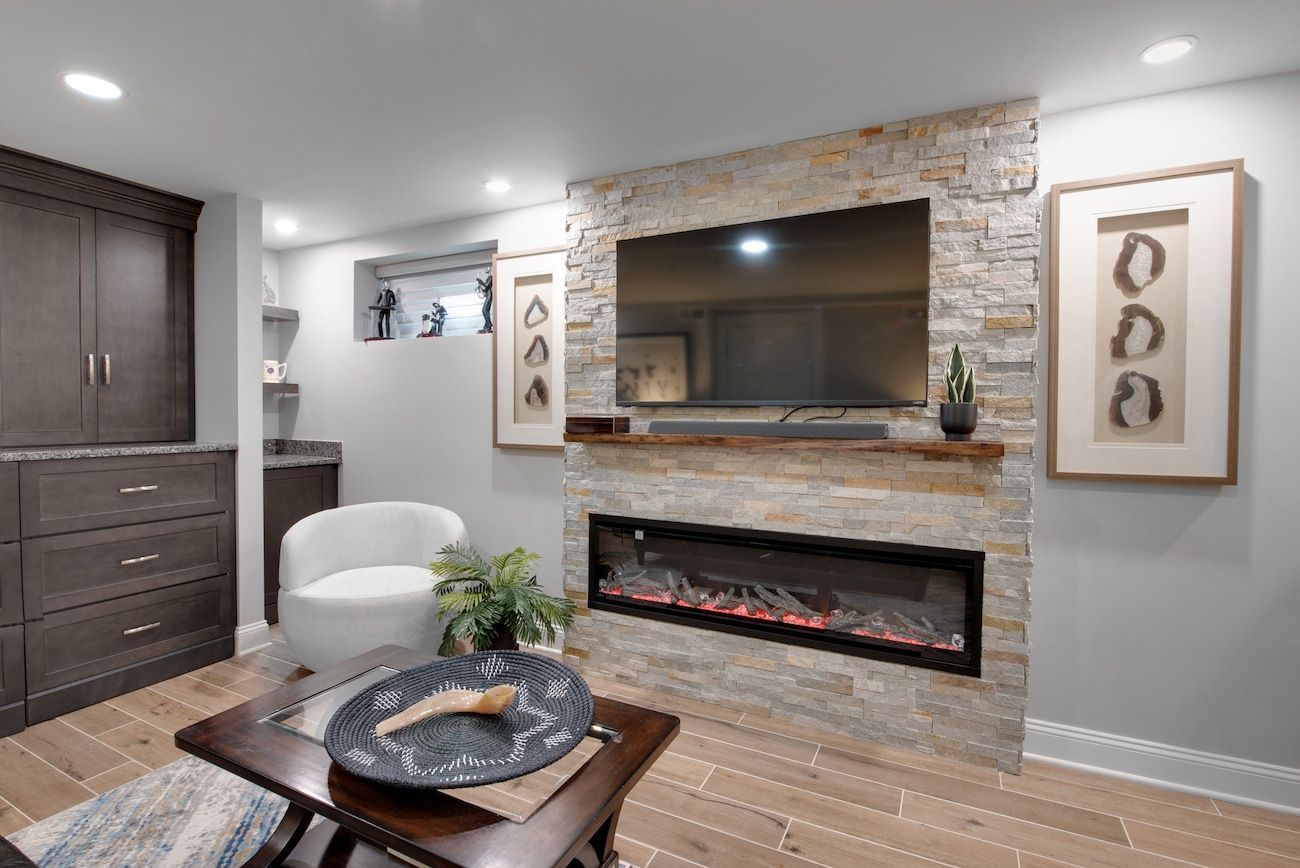 Modern living room with stone fireplace, wall-mounted TV, white chair, and dark coffee table.