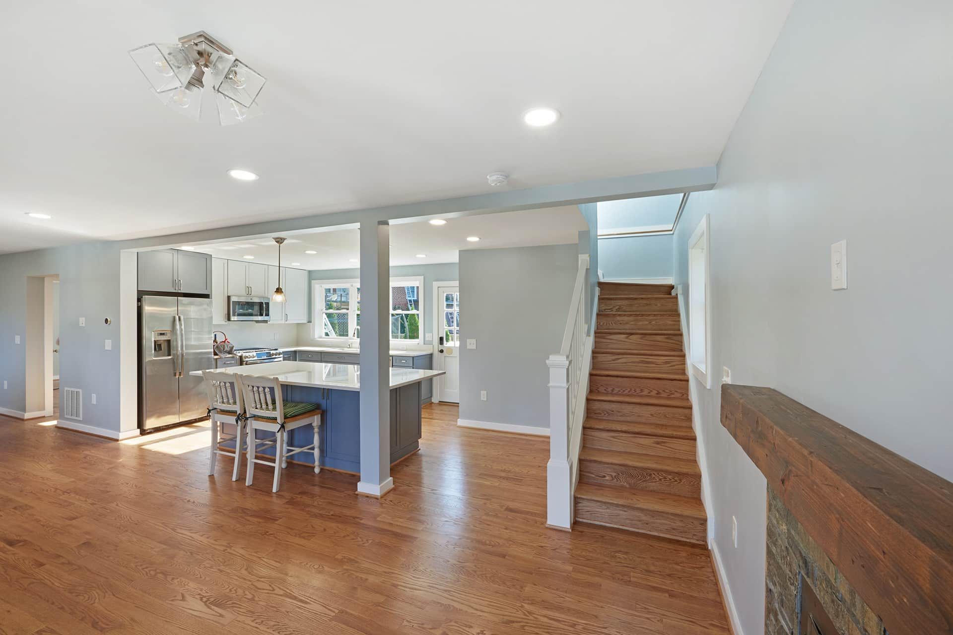 Empty living room with hardwood floors, fireplace, dining area, kitchen island, and staircase