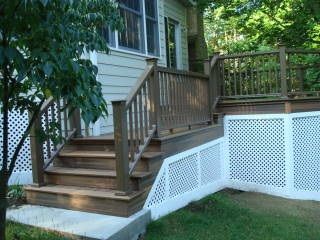 Wooden deck stairs leading to a house, with white lattice skirting and a green lawn below