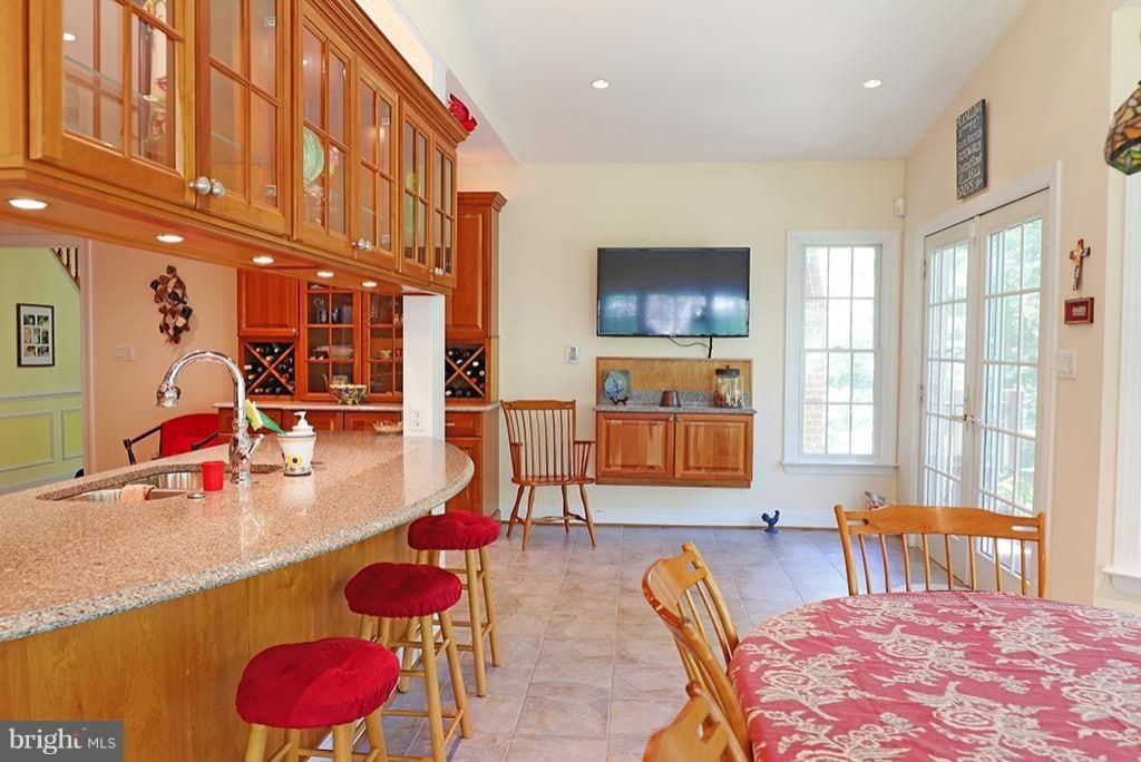 Bright kitchen and dining area with wood cabinets, red stools, a wall TV, and a floral tablecloth
