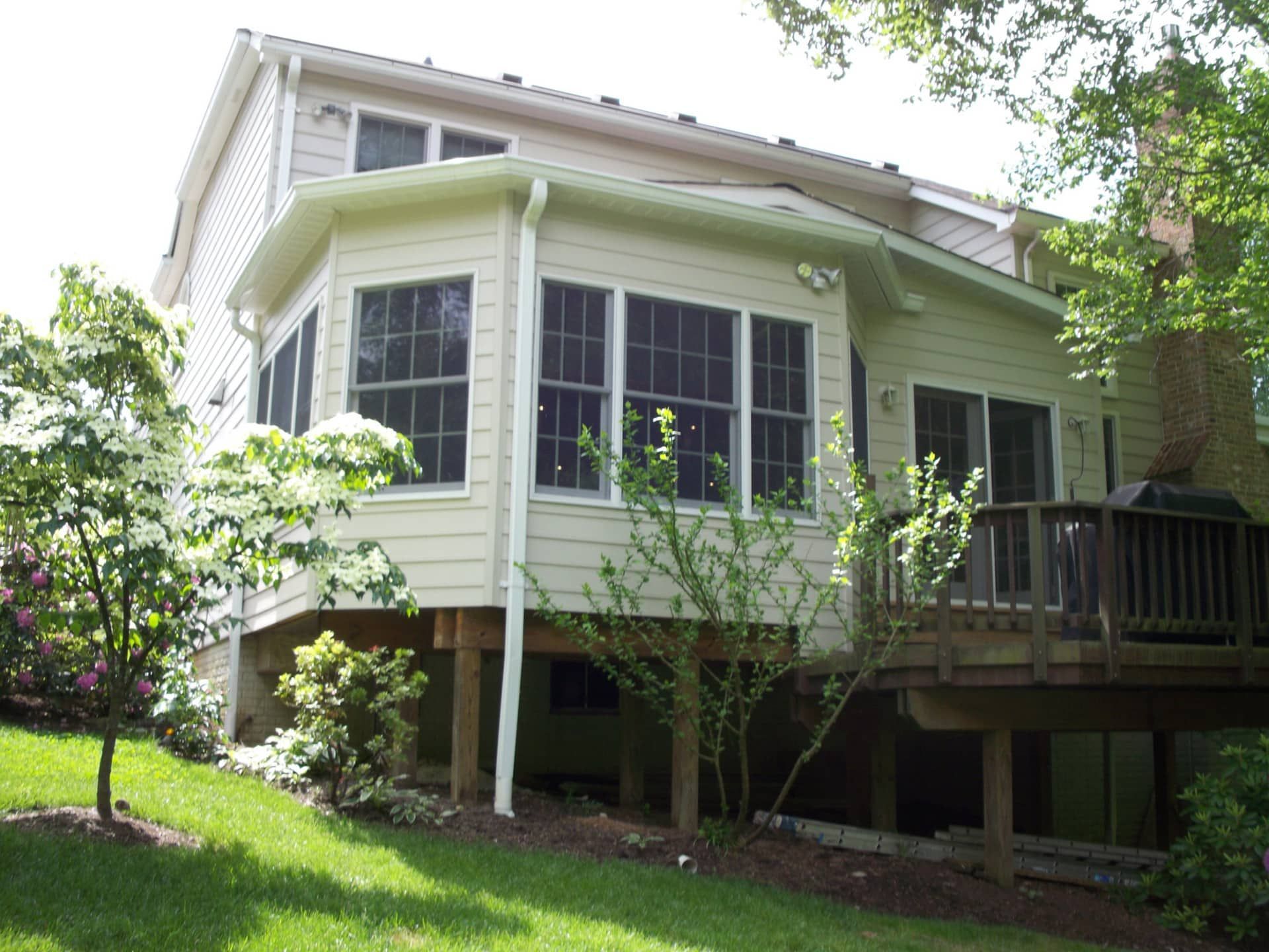 White house with large windows and a wooden deck, surrounded by green lawn and trees.