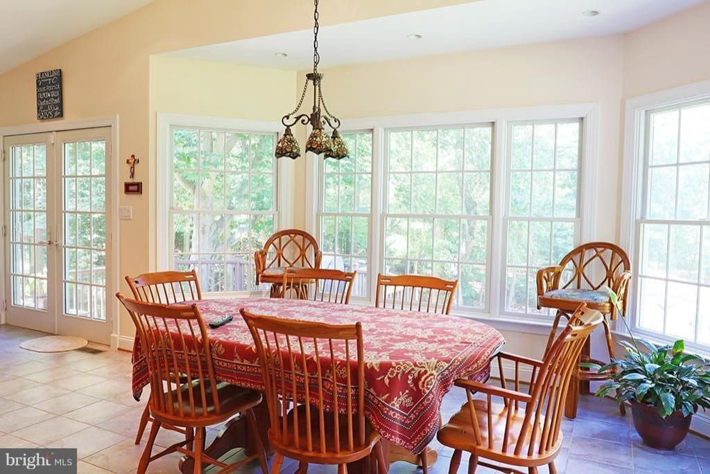 Bright sunroom dining area with wooden table, chairs, red tablecloth, and large windows.