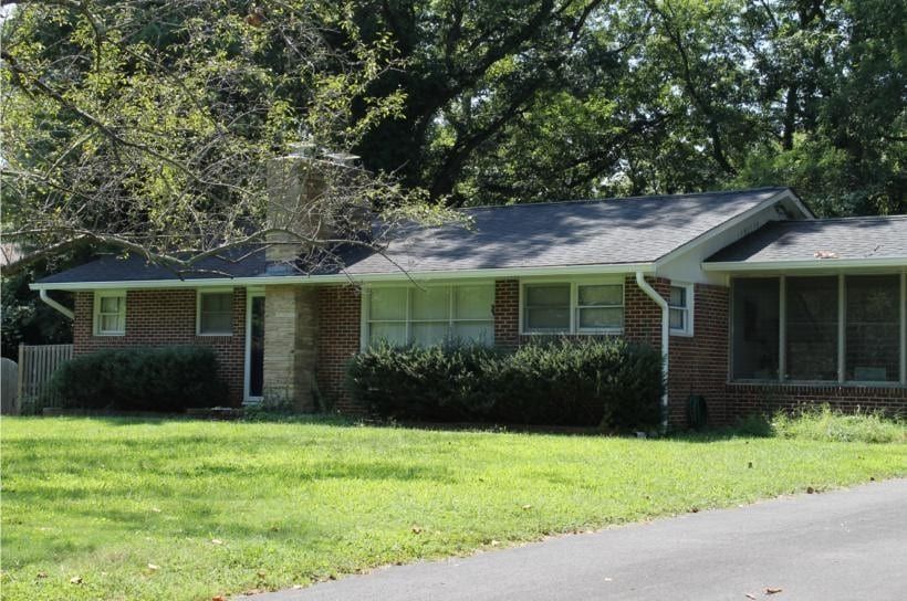 Single-story brick house with green shutters, front lawn, and trees in the yard.