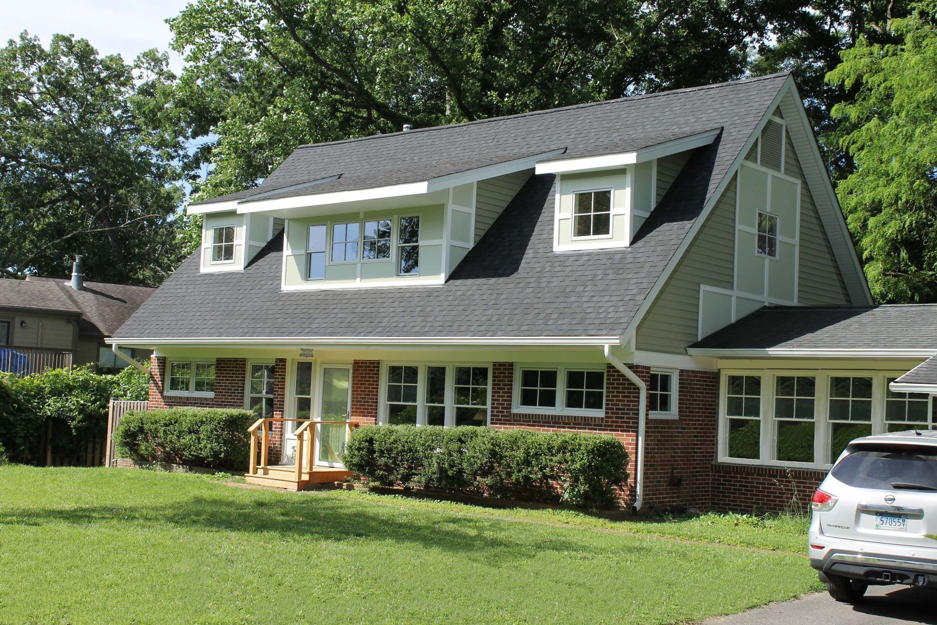 Suburban two-story house with gray roof, white siding, brick porch, and a white SUV in the driveway