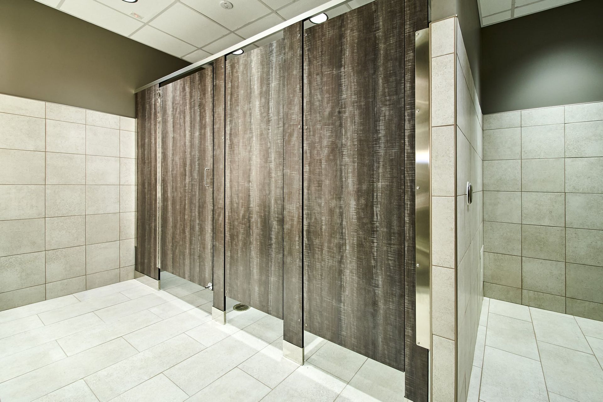 Public restroom with gray stall curtains, tiled walls, and bright overhead lighting