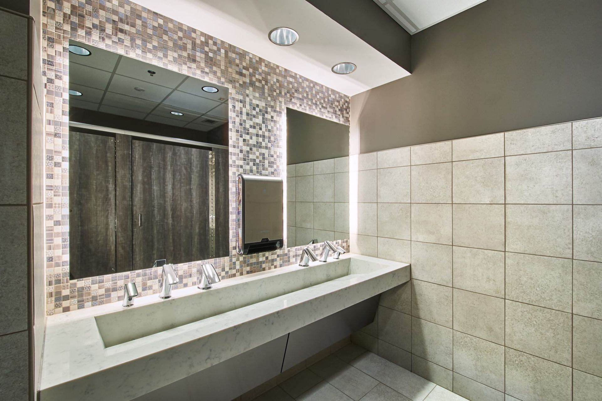 Modern restroom with long mirror, concrete sink counter, and gray tiled walls