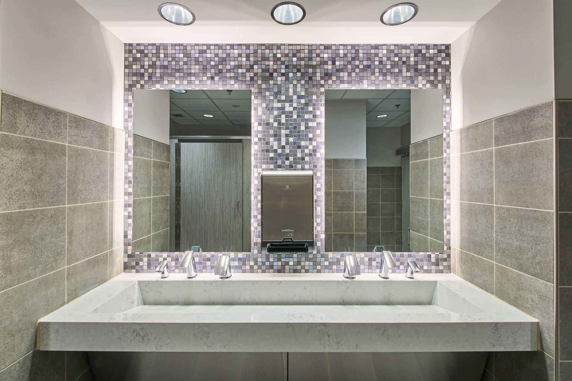 Modern bathroom vanity with mosaic-framed mirrors, white sink, and gray tile walls