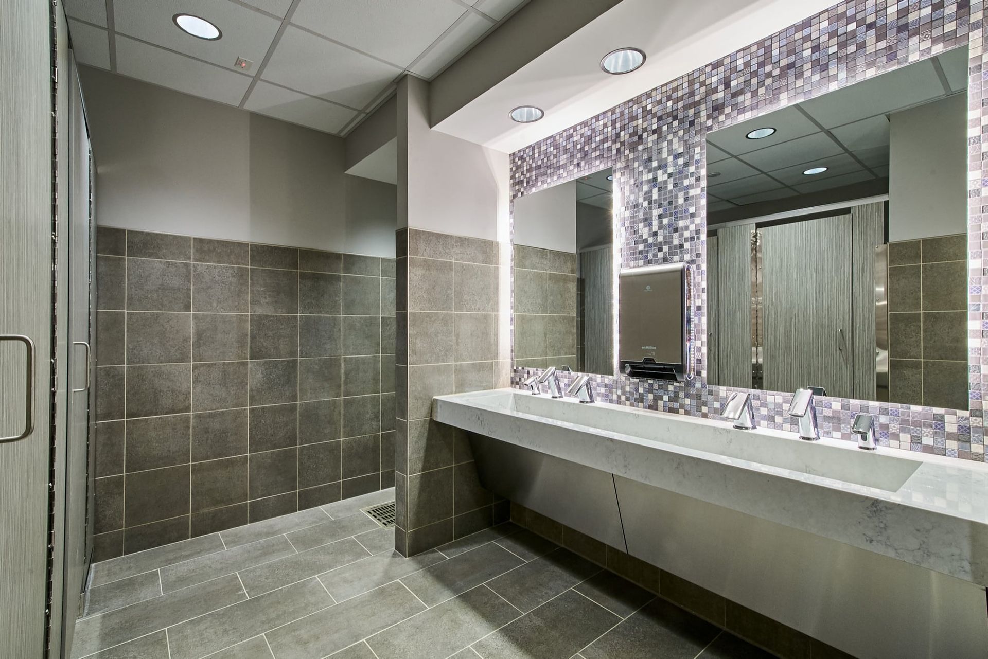 Modern public restroom with gray tile, a long sink counter, and large mirrors.