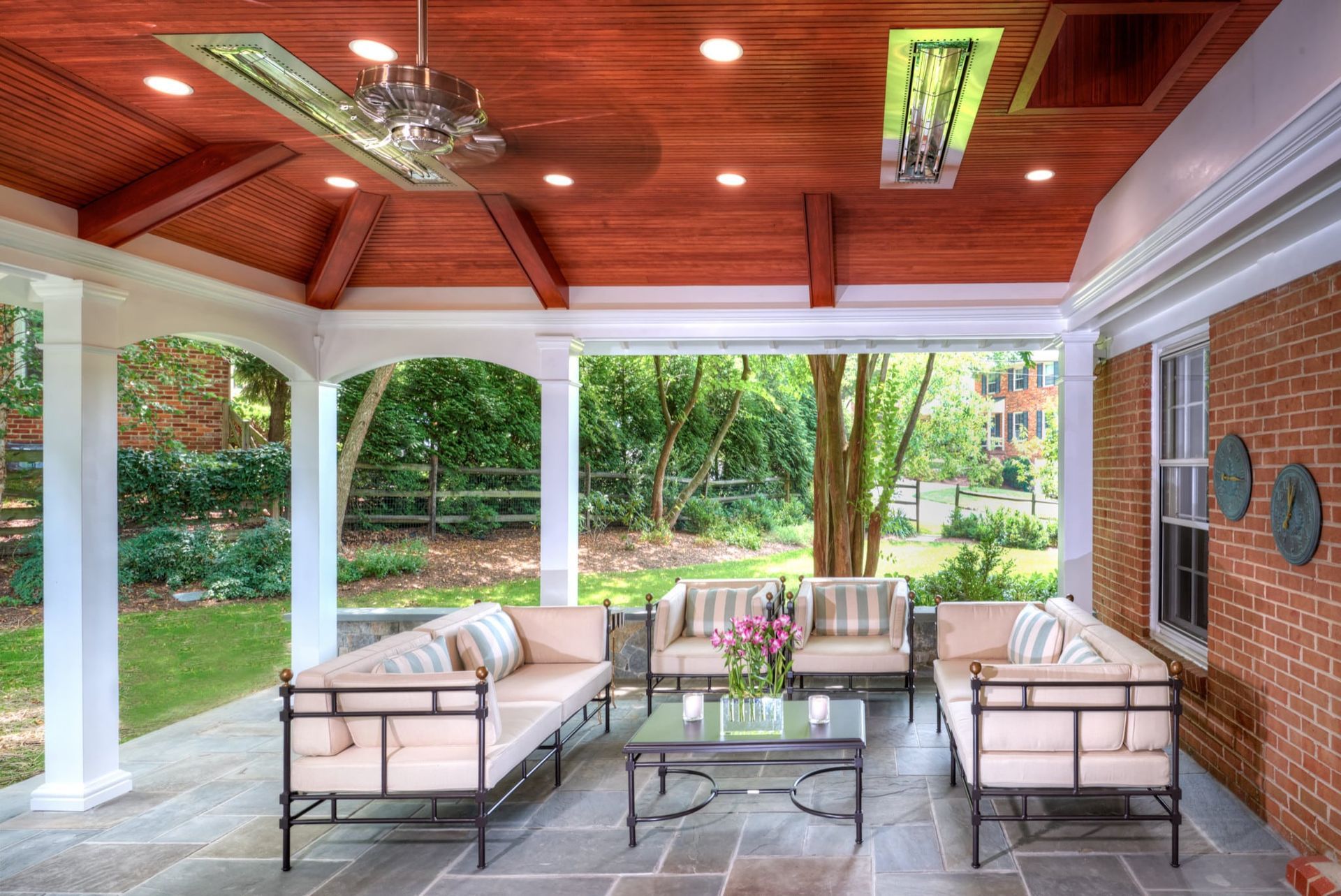 Covered patio with cream sofas, glass table, brick wall, and views of a lush garden