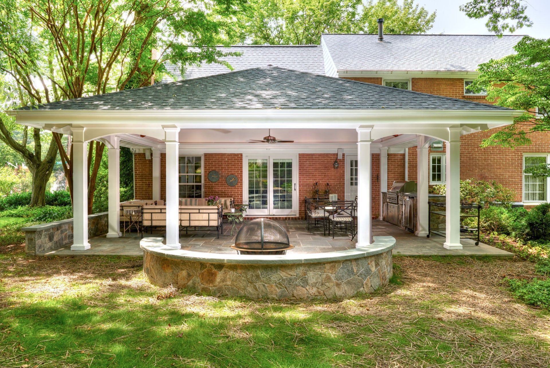Brick house porch with white columns, green roof, and a curved stone patio surrounded by trees