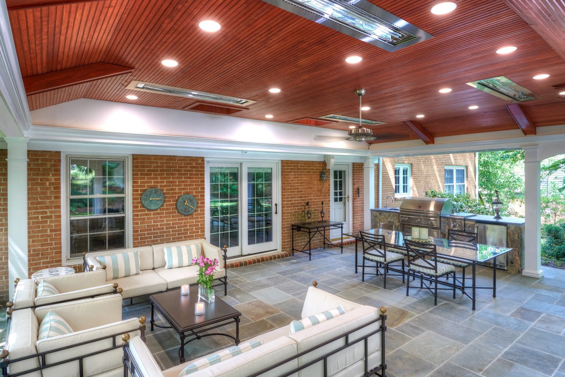 Spacious covered patio with wicker seating, dining tables, brick walls, and a wood-paneled ceiling.