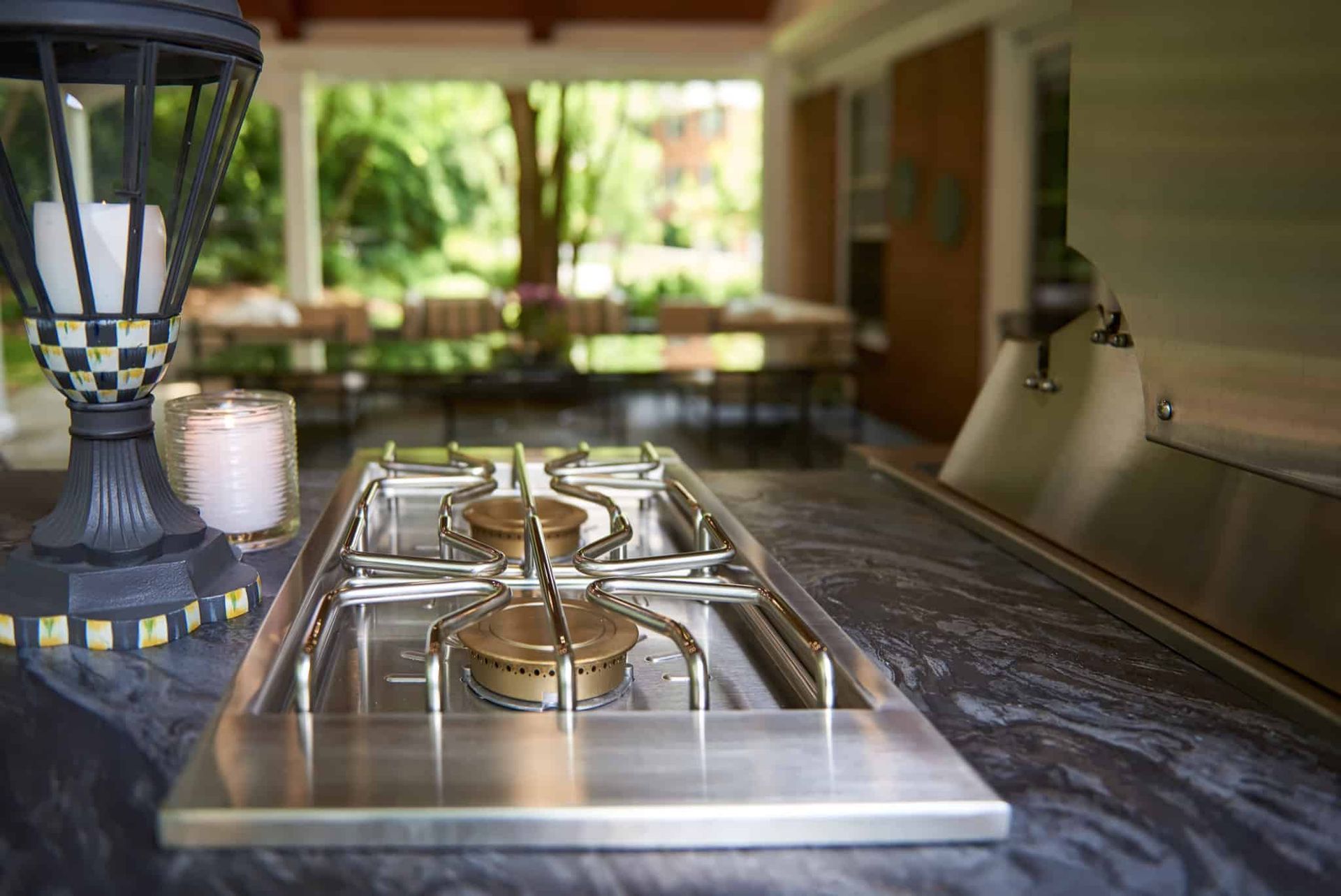 Outdoor patio with stainless steel gas grill on a stone counter and blurred backyard seating in the background