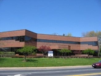 Low-rise brick office building with dark windows and a lawn in front on a sunny day