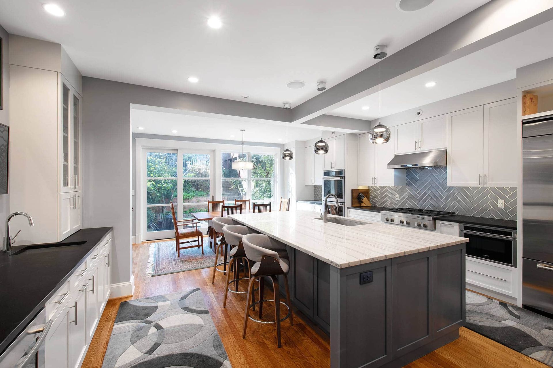 Modern open-plan kitchen with island, dark cabinets, white counters, and a dining area by sliding glass doors