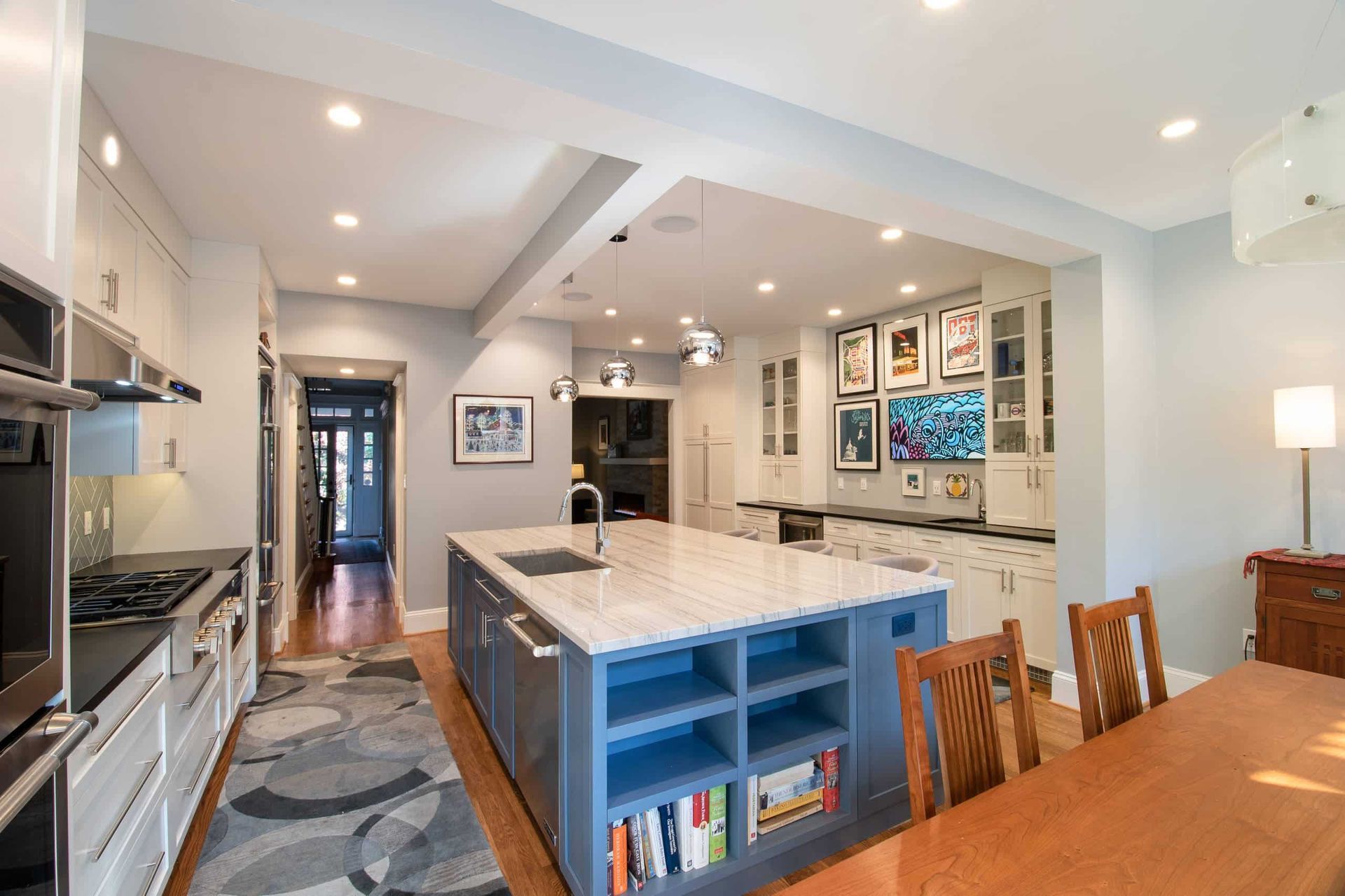 Bright modern kitchen with a large island, white cabinets, blue shelving, and dining table nearby