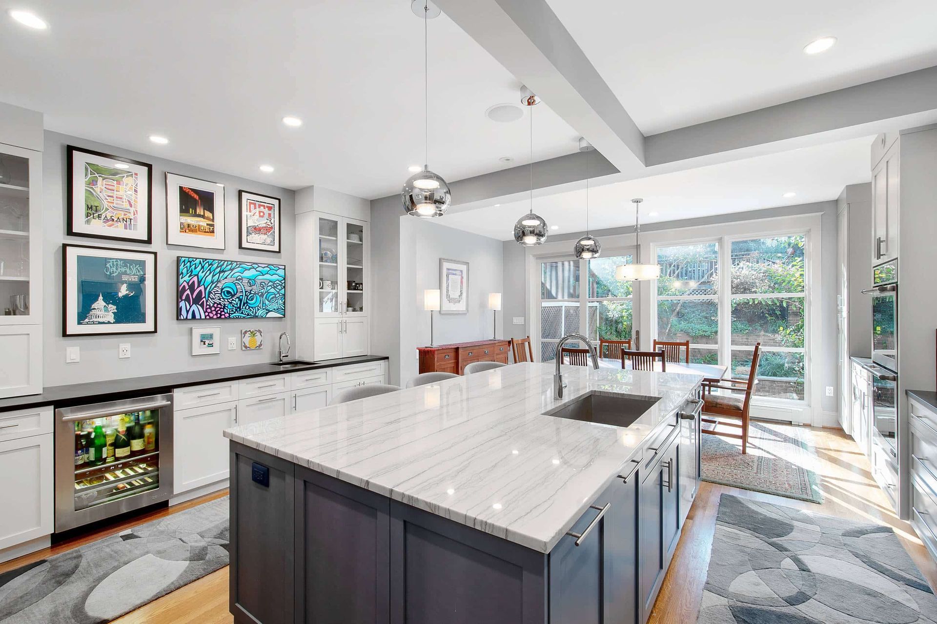 Bright modern kitchen with large island, white cabinets, pendant lights, and dining area by glass doors