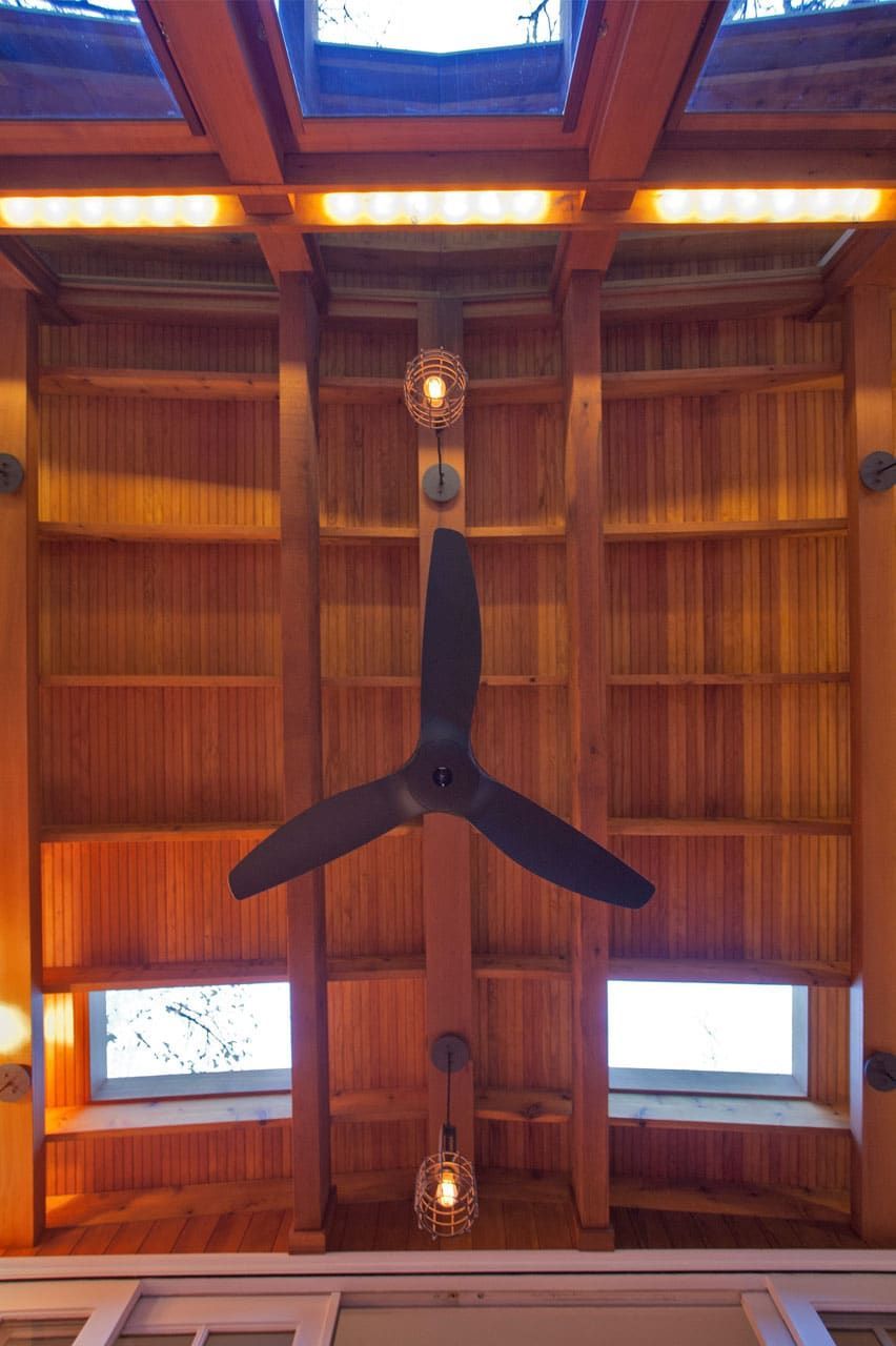 Wood-paneled vaulted ceiling with a large black ceiling fan and skylight windows