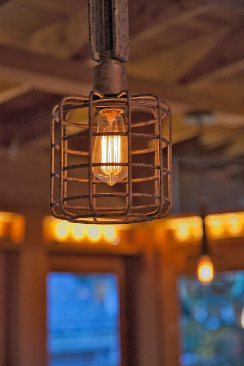 Warm Edison bulb in a wire cage pendant light hanging indoors, with soft ambient glow.