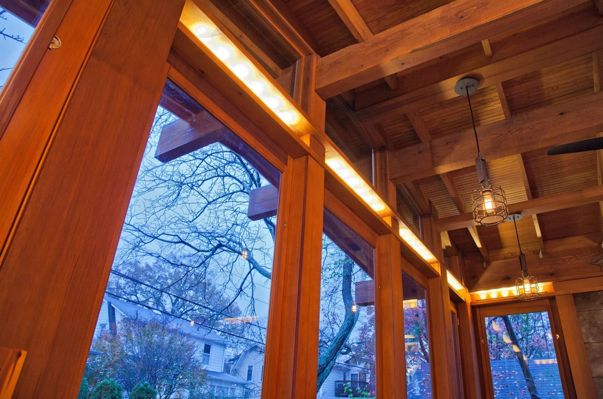Wooden porch with warm lights and large windows overlooking snowy trees at dusk