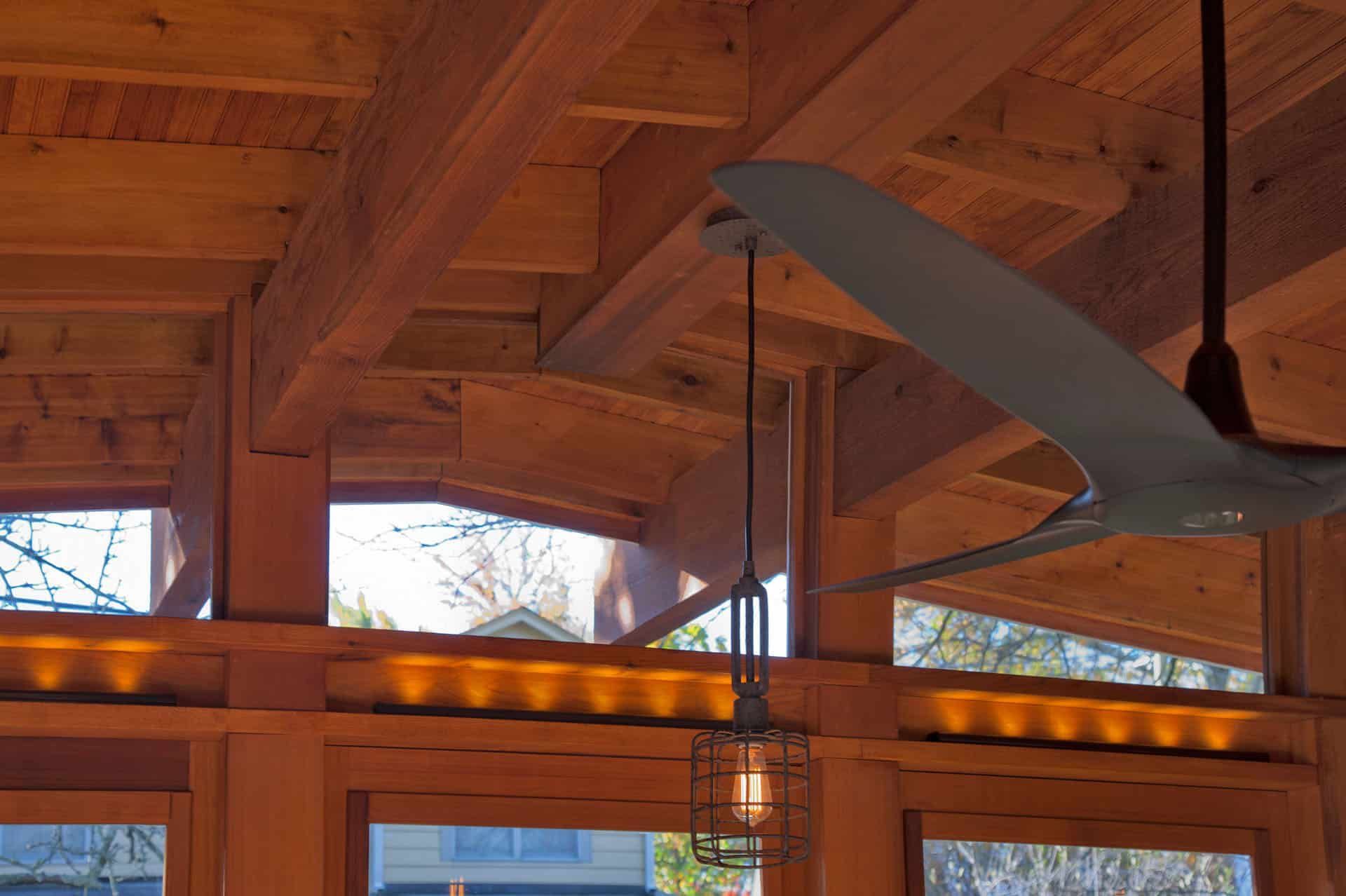 Wooden lodge ceiling with hanging ceiling fans and warm pendant lights above windows