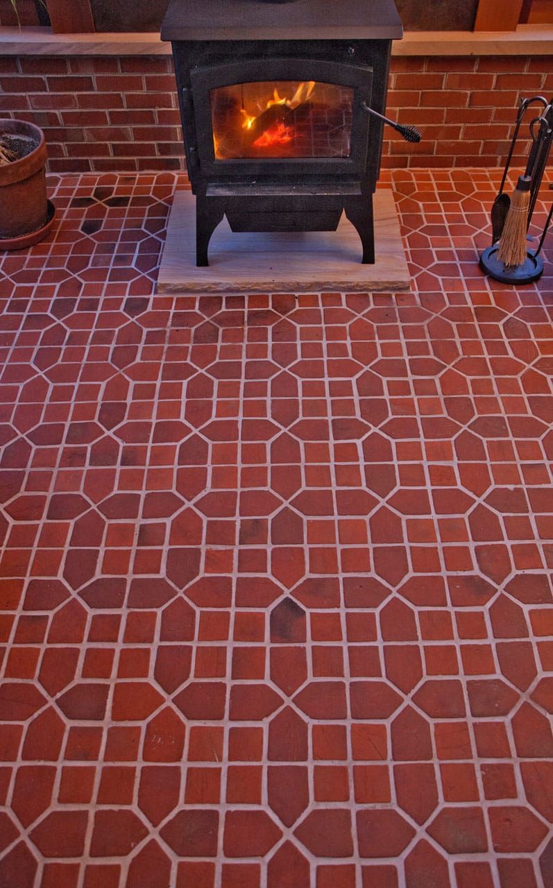 Red tiled patio with a lit black wood stove against a brick wall