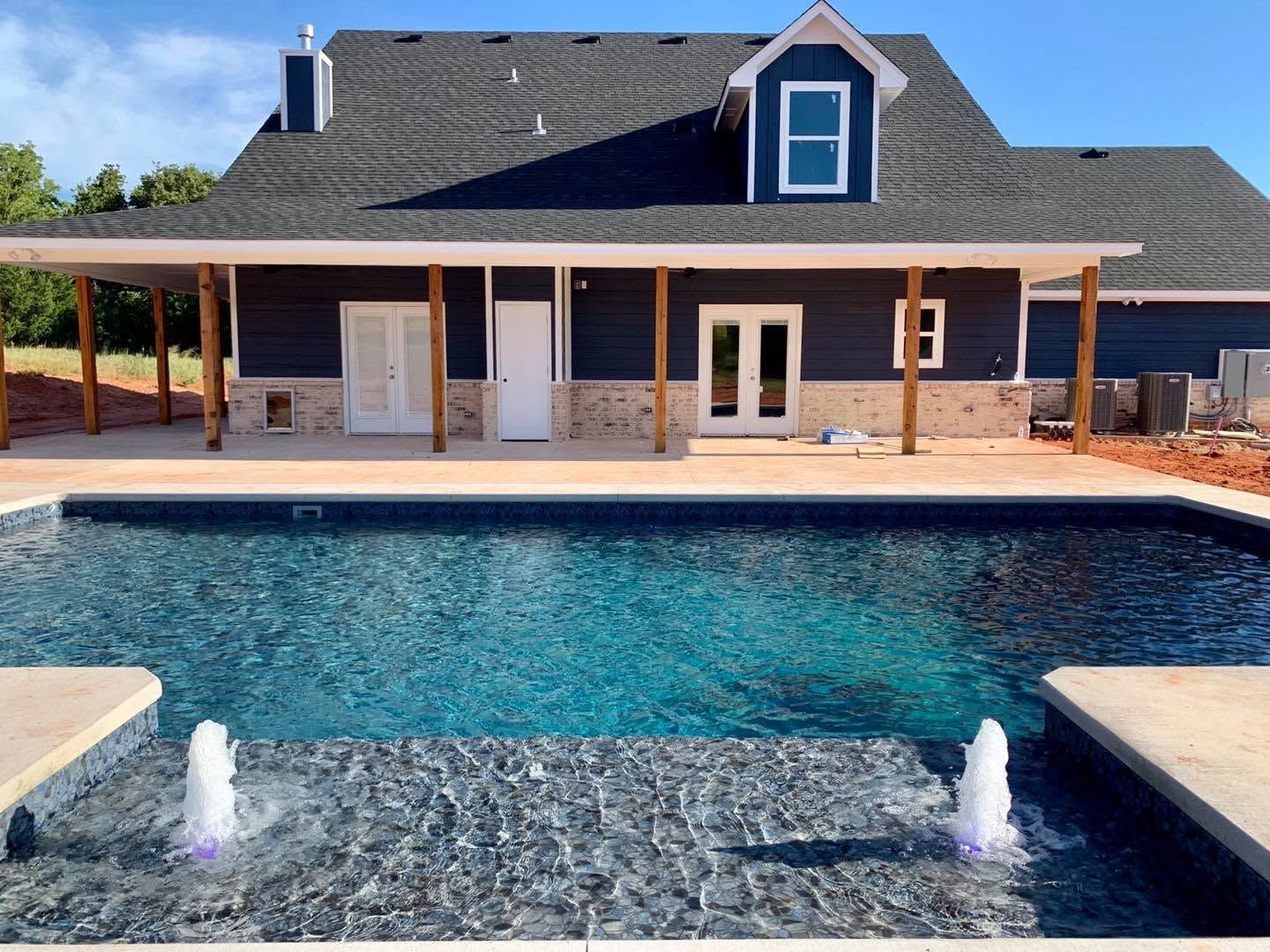 Backyard house with covered patio and a large swimming pool under a blue sky