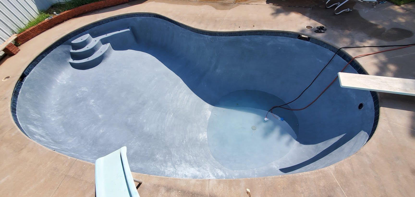 Empty blue swimming pool with a built-in hot tub, viewed from above.