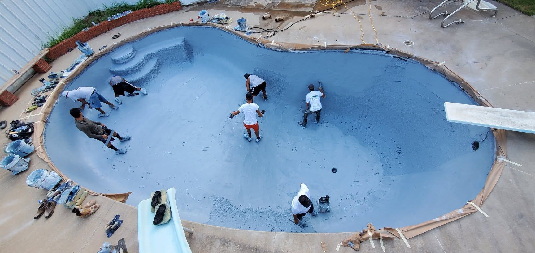 Workers spreading blue concrete in a pool foundation under construction