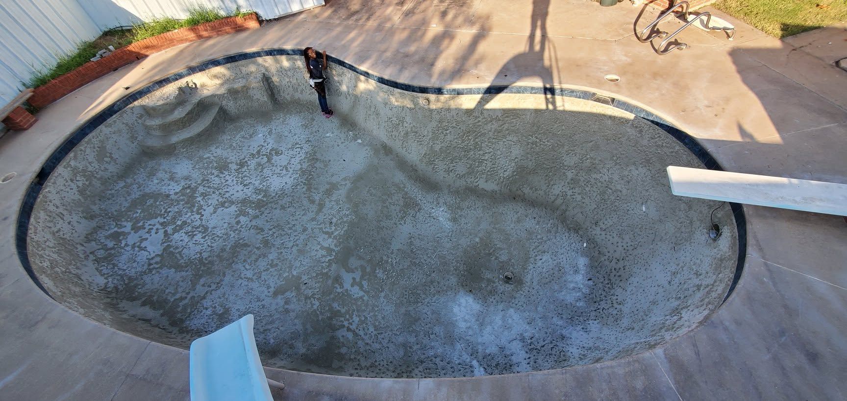 Empty swimming pool with gray concrete interior and a white pipe extending in from the right