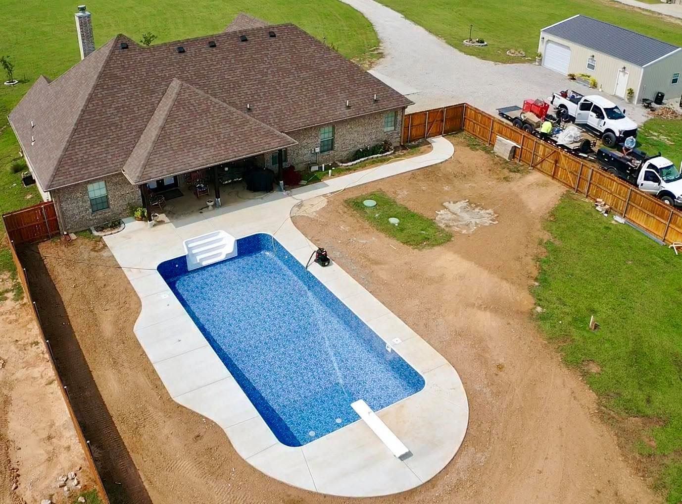 Aerial view of a backyard with a covered rectangular pool beside a house and fenced yard