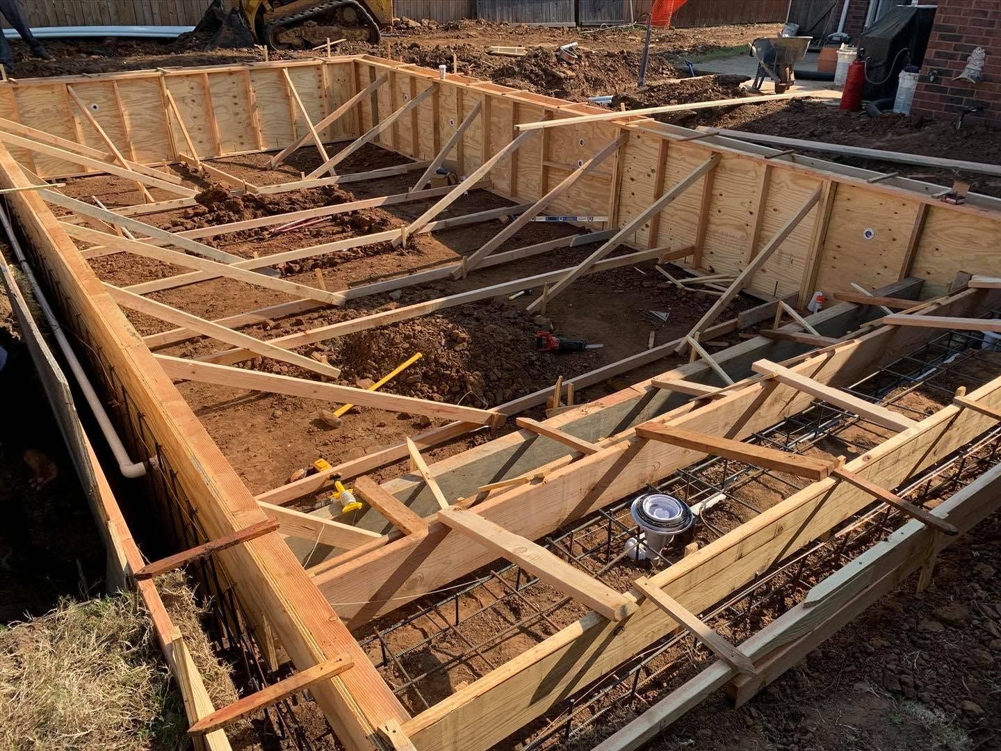 Wooden formwork for a concrete foundation at a construction site, with rebar and dirt inside.