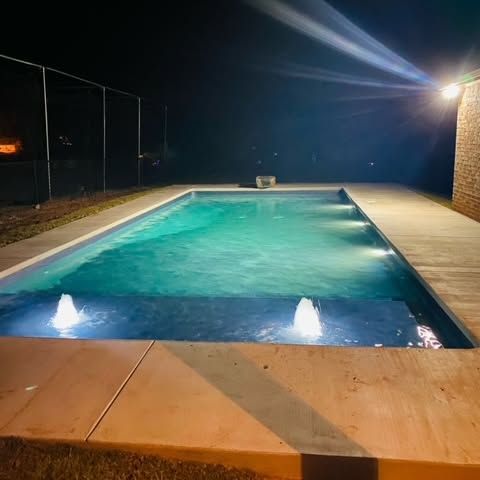 Nighttime backyard pool with turquoise water, deck lights, and bright wall light beams