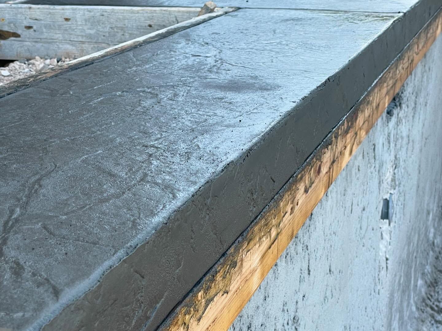 Close-up of a concrete ledge with a dark gray top and weathered blue wall below.