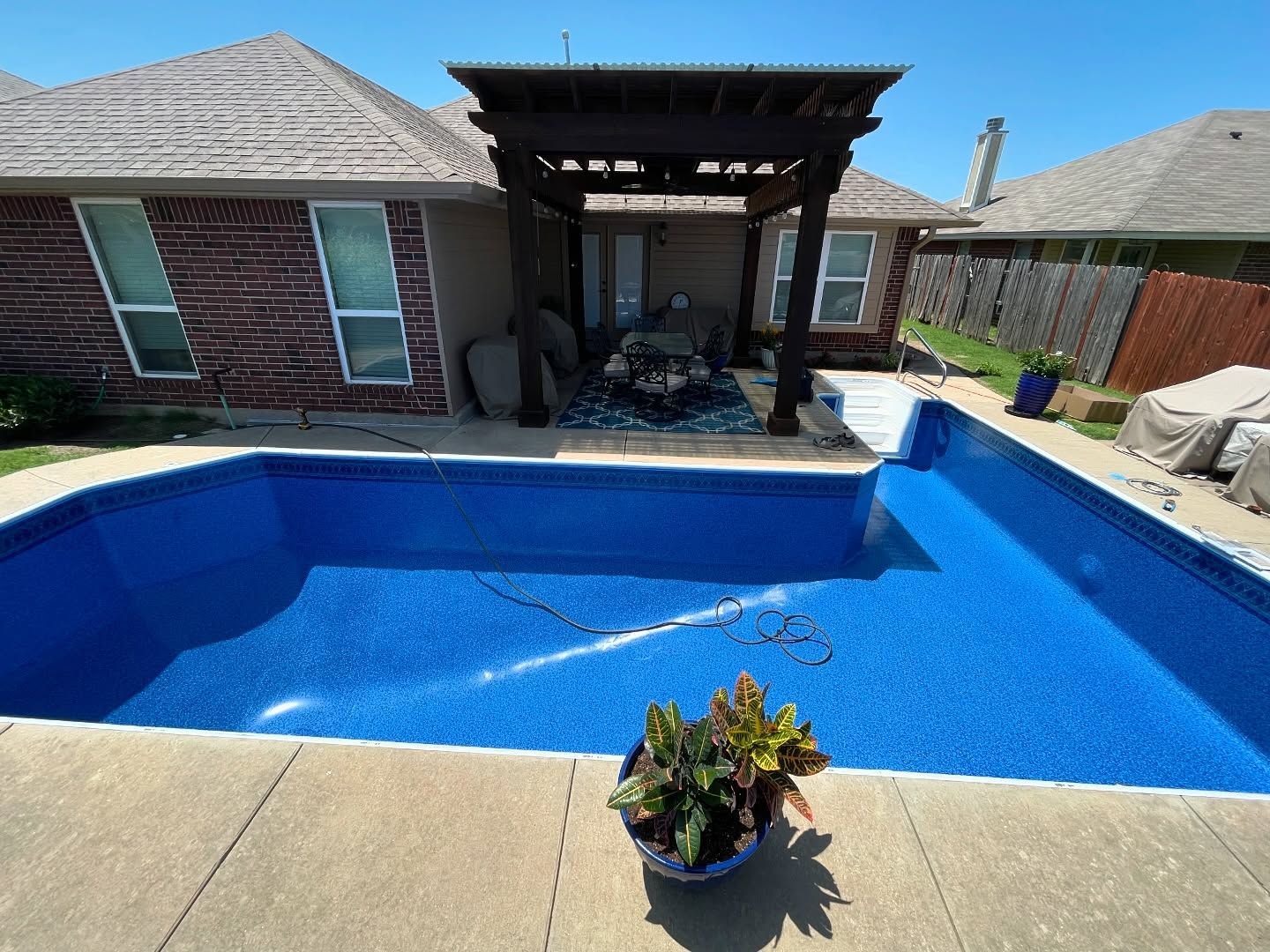 Backyard pool with blue water beside a brick house and covered patio.