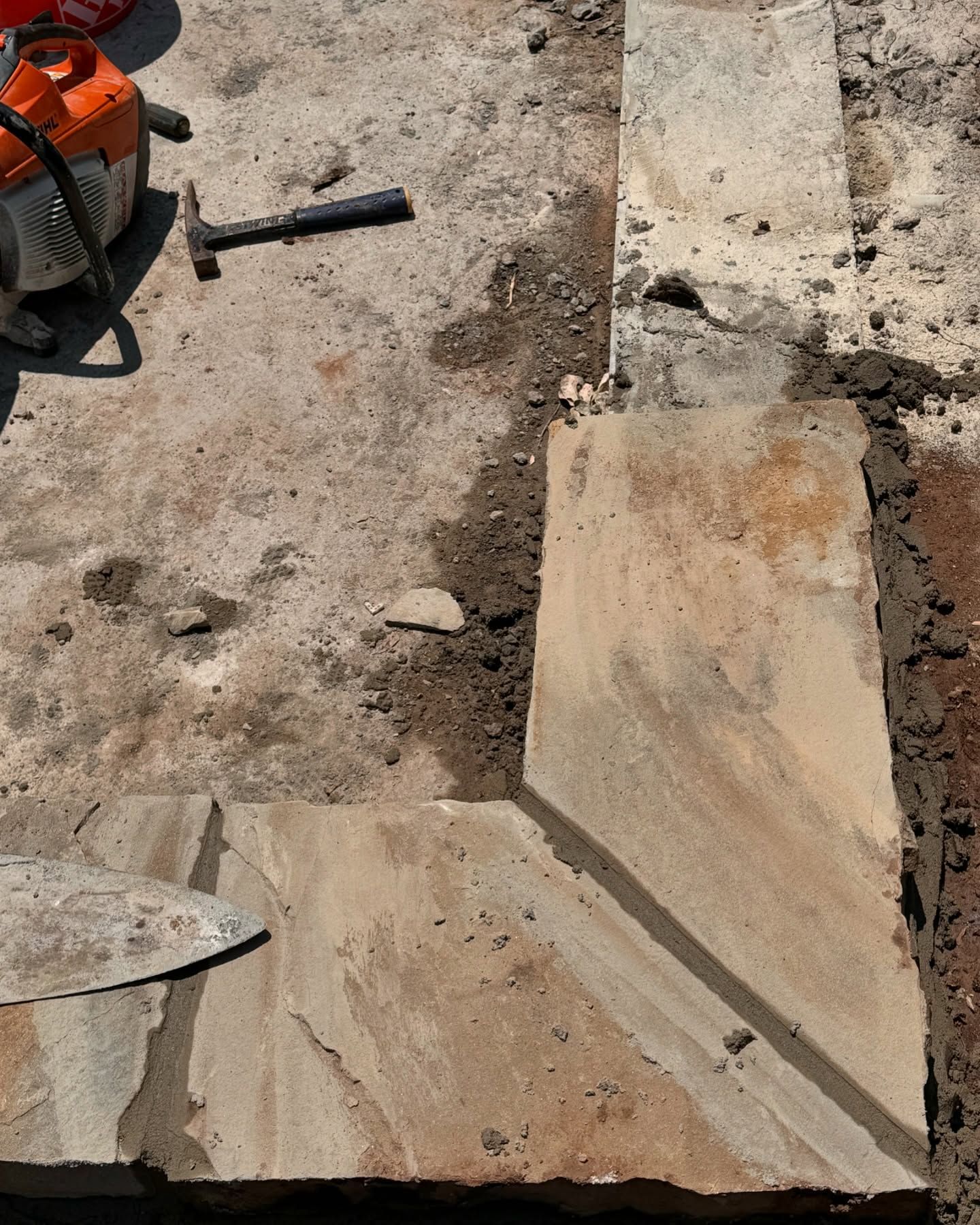 Stone pavement under construction with a trowel and orange tool on a rough concrete surface