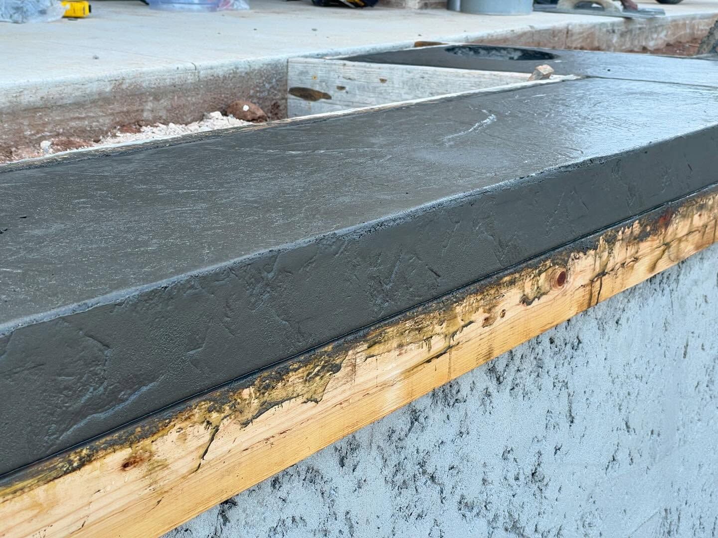 Weathered concrete curb with black sealant and peeling yellow trim on a blue wall