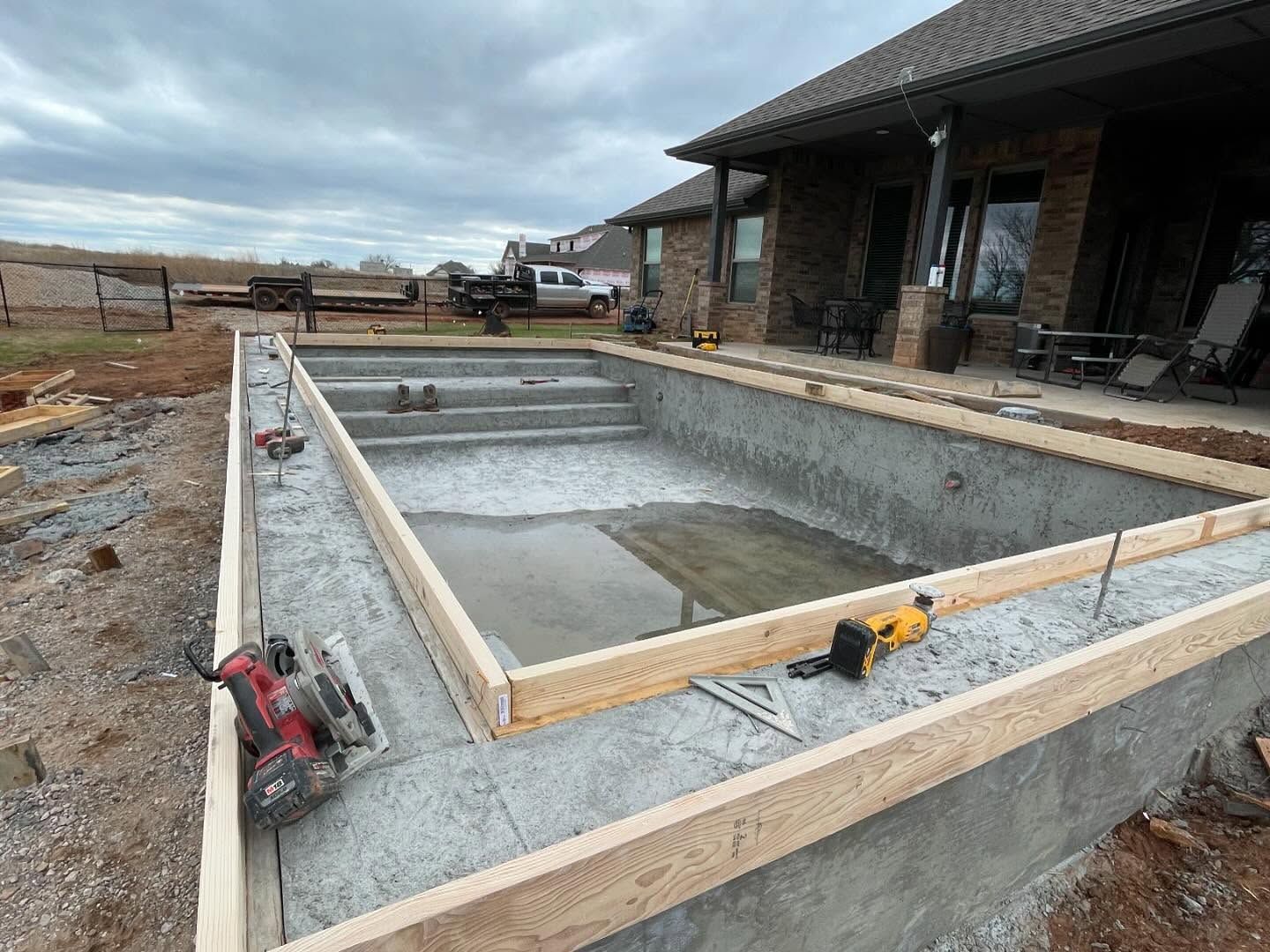 Partially built concrete pool with wooden framing beside a house under construction