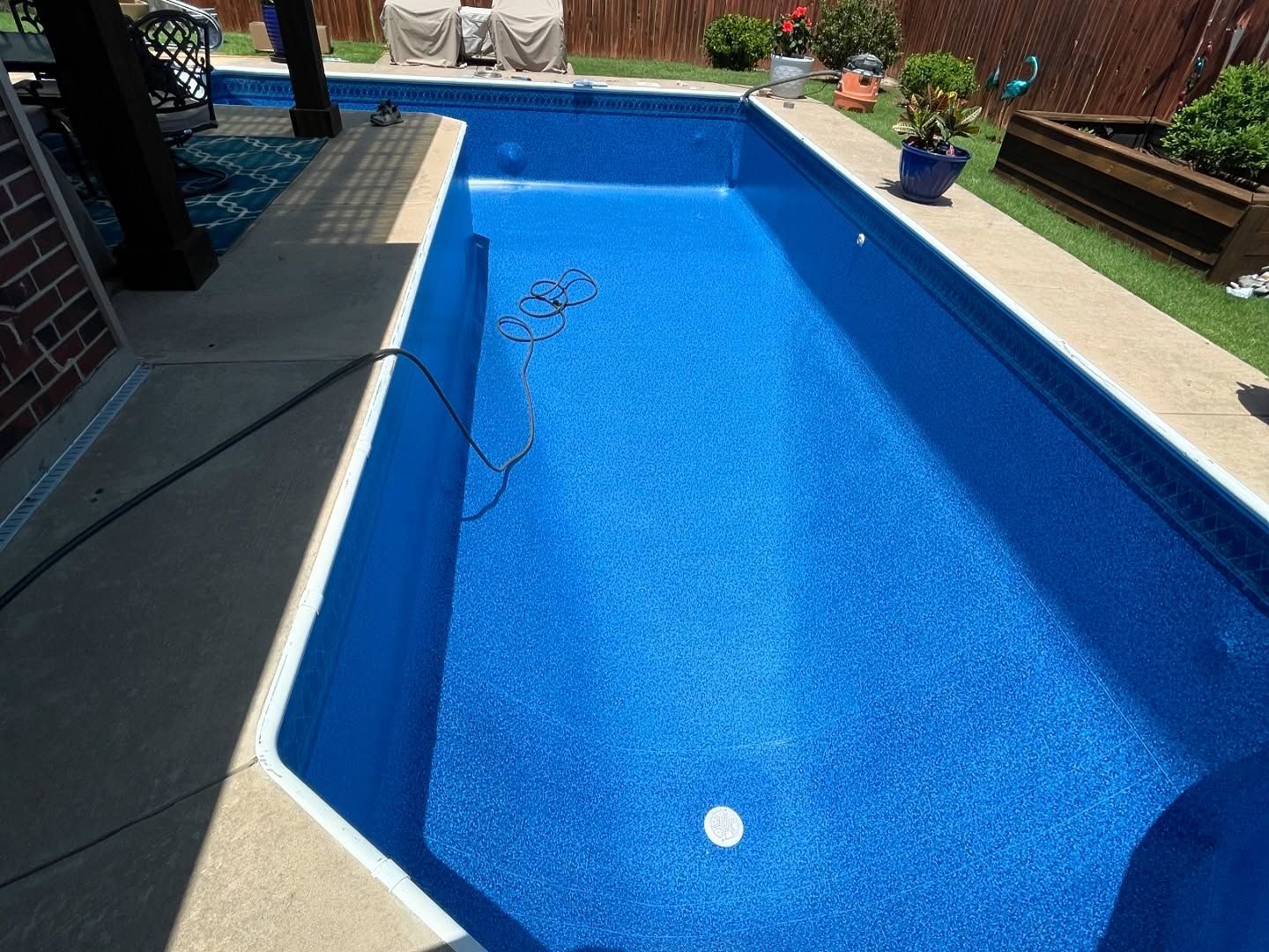Backyard swimming pool with blue water, white coping, and a hose on the deck