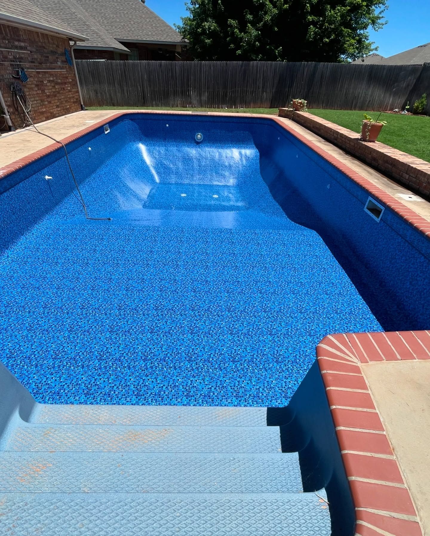 Backyard swimming pool with blue water, brick coping, and steps in the foreground