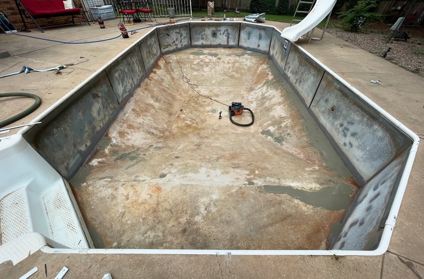 Empty octagonal in-ground pool shell with worn concrete interior and a drain in the center