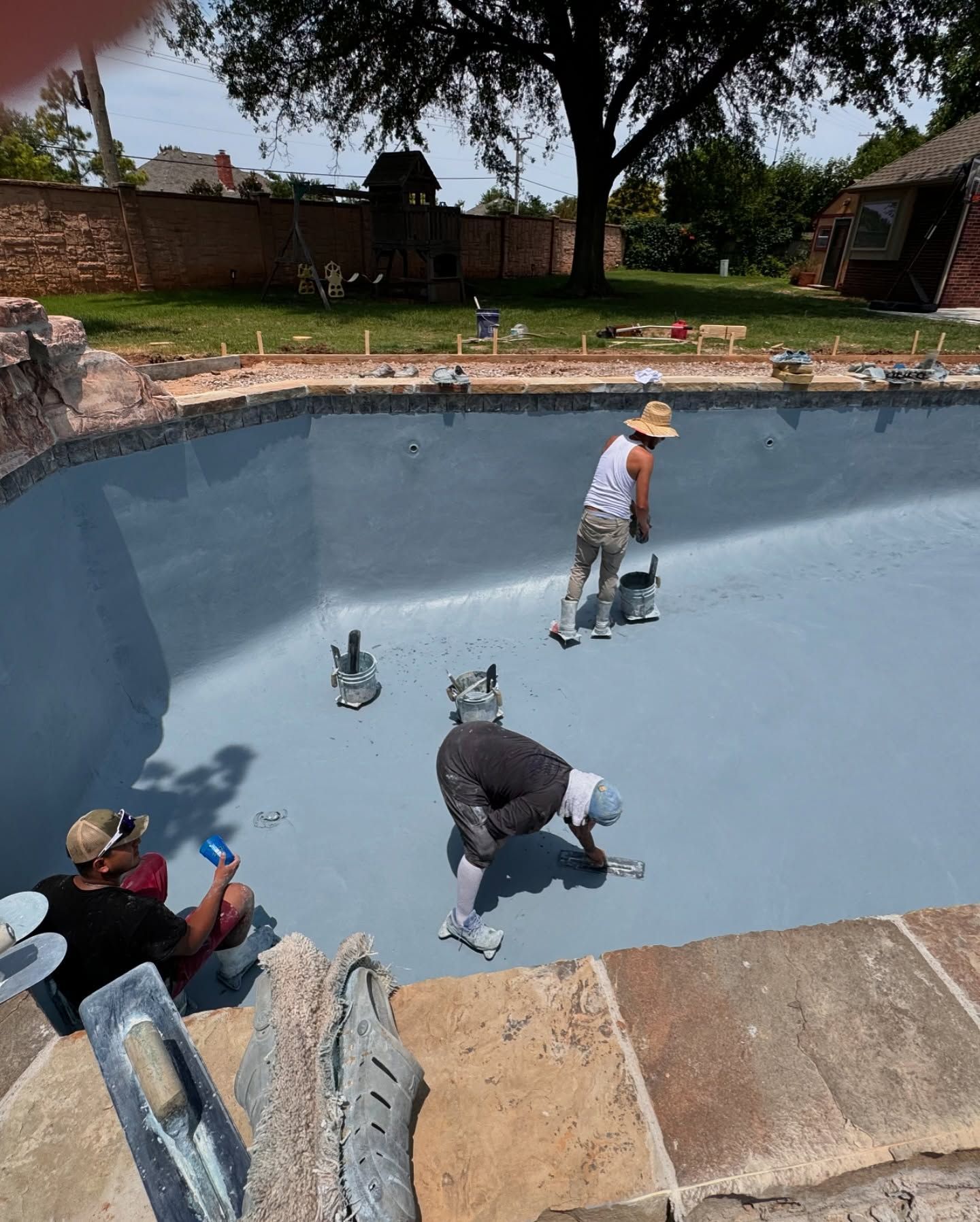 Workers painting an empty blue swimming pool with brushes and rollers outdoors