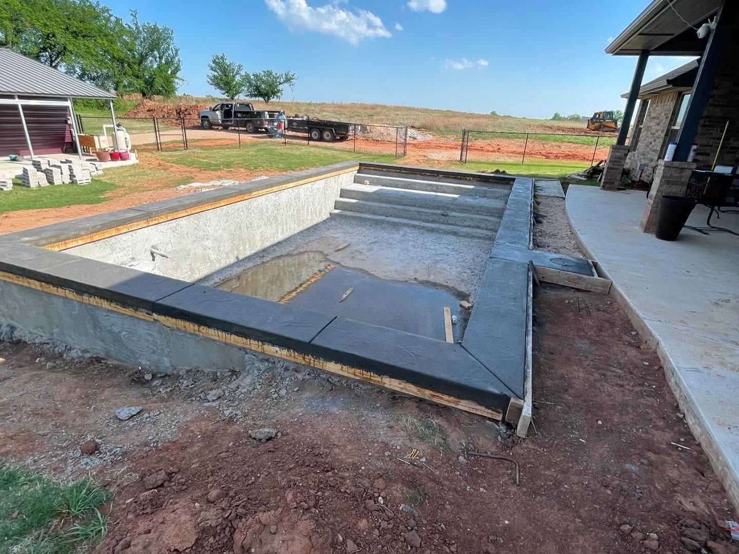 Backyard in-ground pool under construction with concrete deck and excavation area