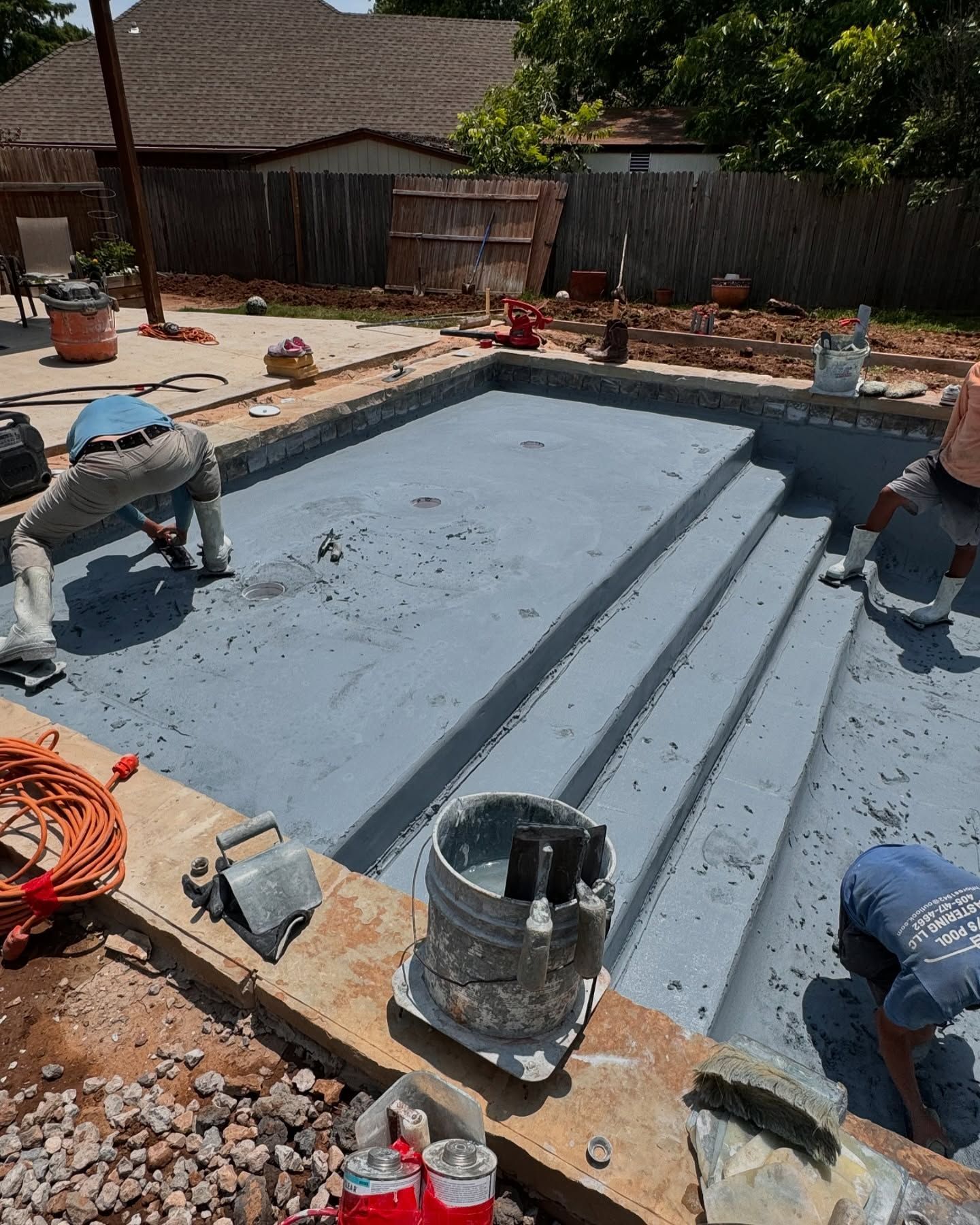 Workers coating a gray backyard swimming pool during construction