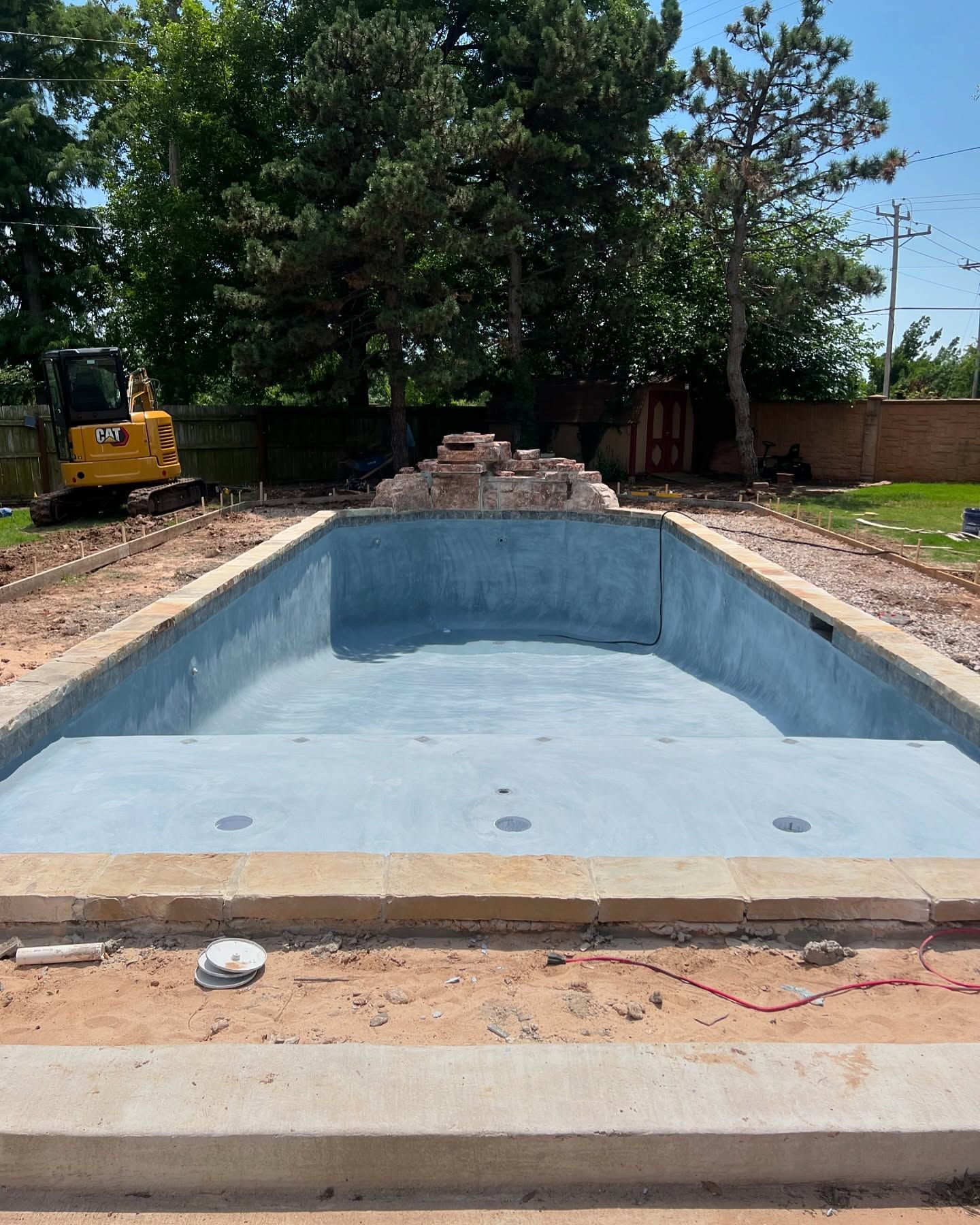 Empty backyard swimming pool under construction with light blue interior and dirt piles around it