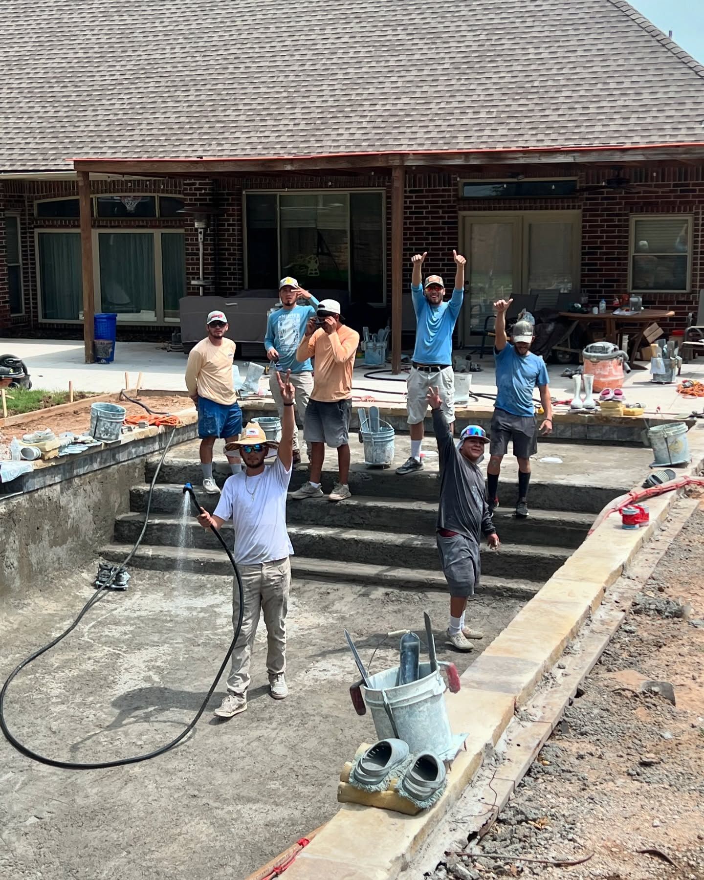 Workers in a yard with a newly finished pool, some raising their arms near a house.